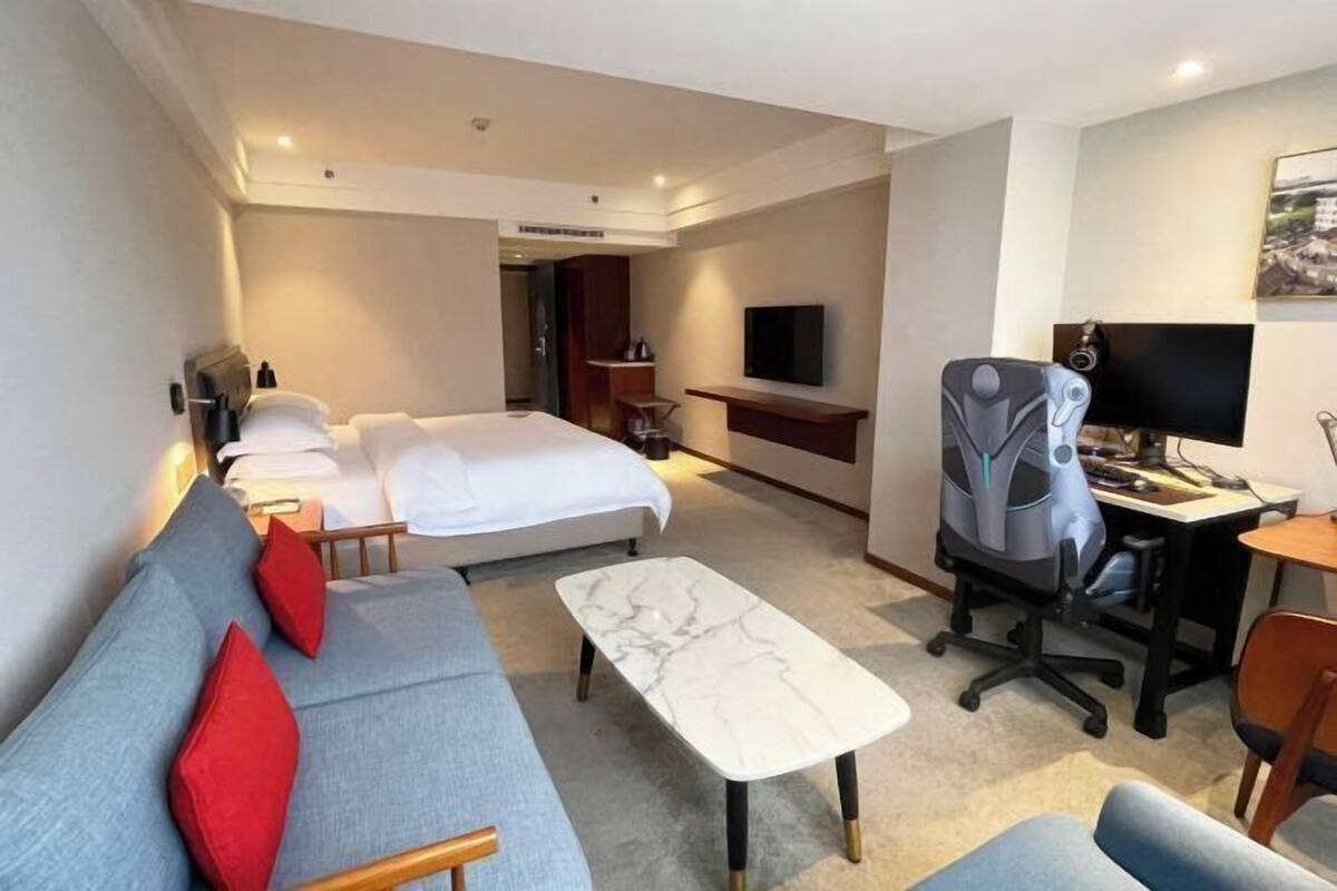 Una habitación de hotel con cama, sofá, escritorio con computadora, televisión y una silla.