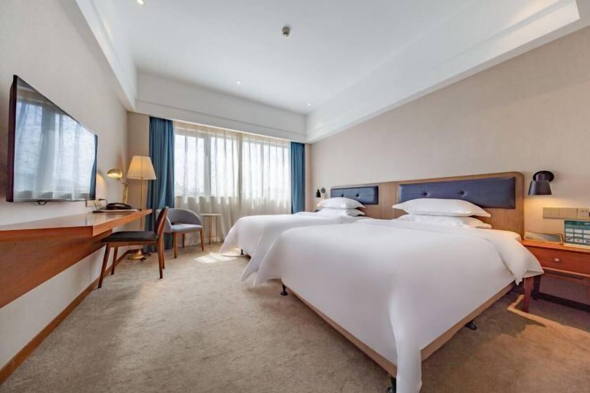 Habitación de hotel con dos camas, un escritorio, una silla, un televisor y una ventana con cortinas.