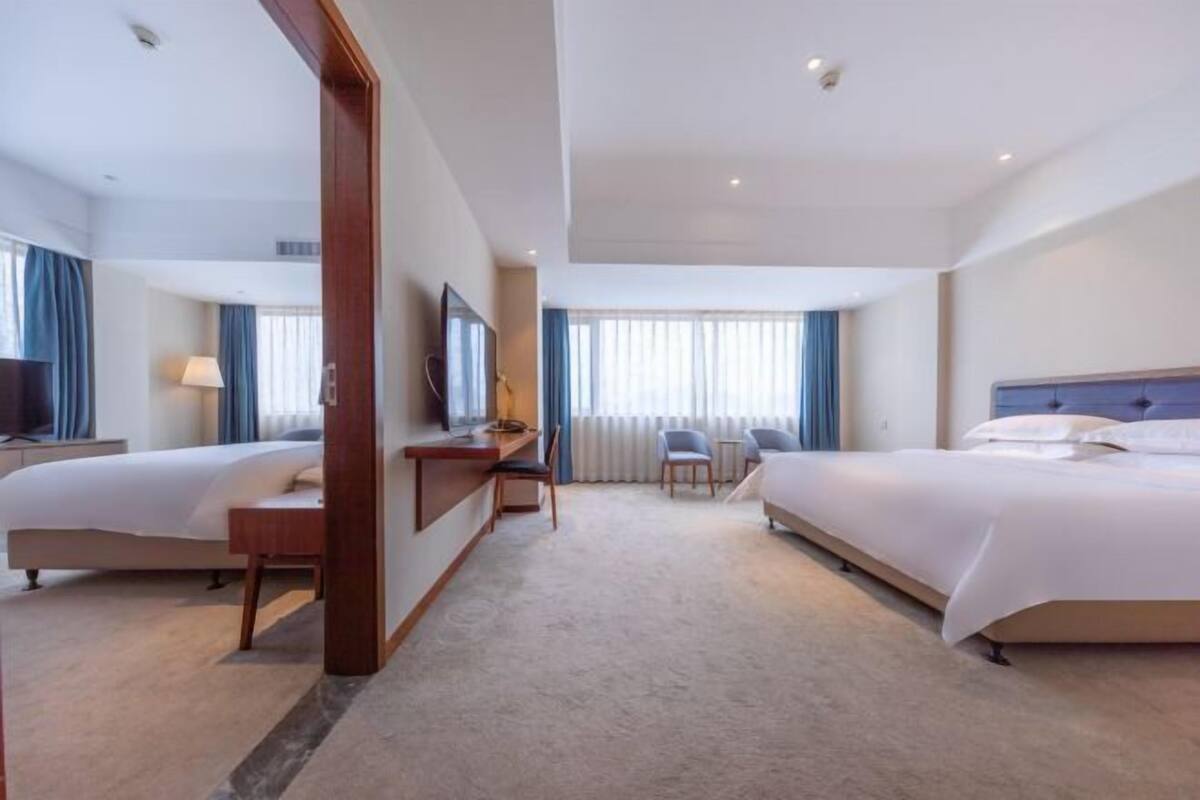 Habitación de hotel con dos camas, un escritorio, una silla, un televisor y una ventana con cortinas.