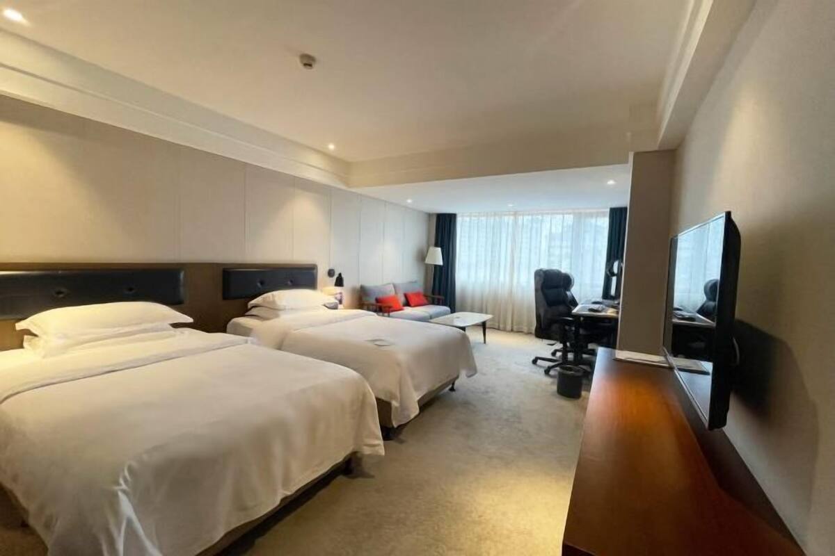 Habitación de hotel con dos camas, un escritorio, una silla, un televisor y una ventana con cortinas.