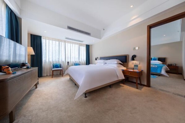 A hotel room with a bed, a desk, a chair, a TV, and a large mirror.