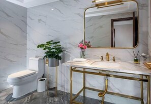 A bathroom with a marble wall, a gold-framed sink, a toilet, and a potted plant.