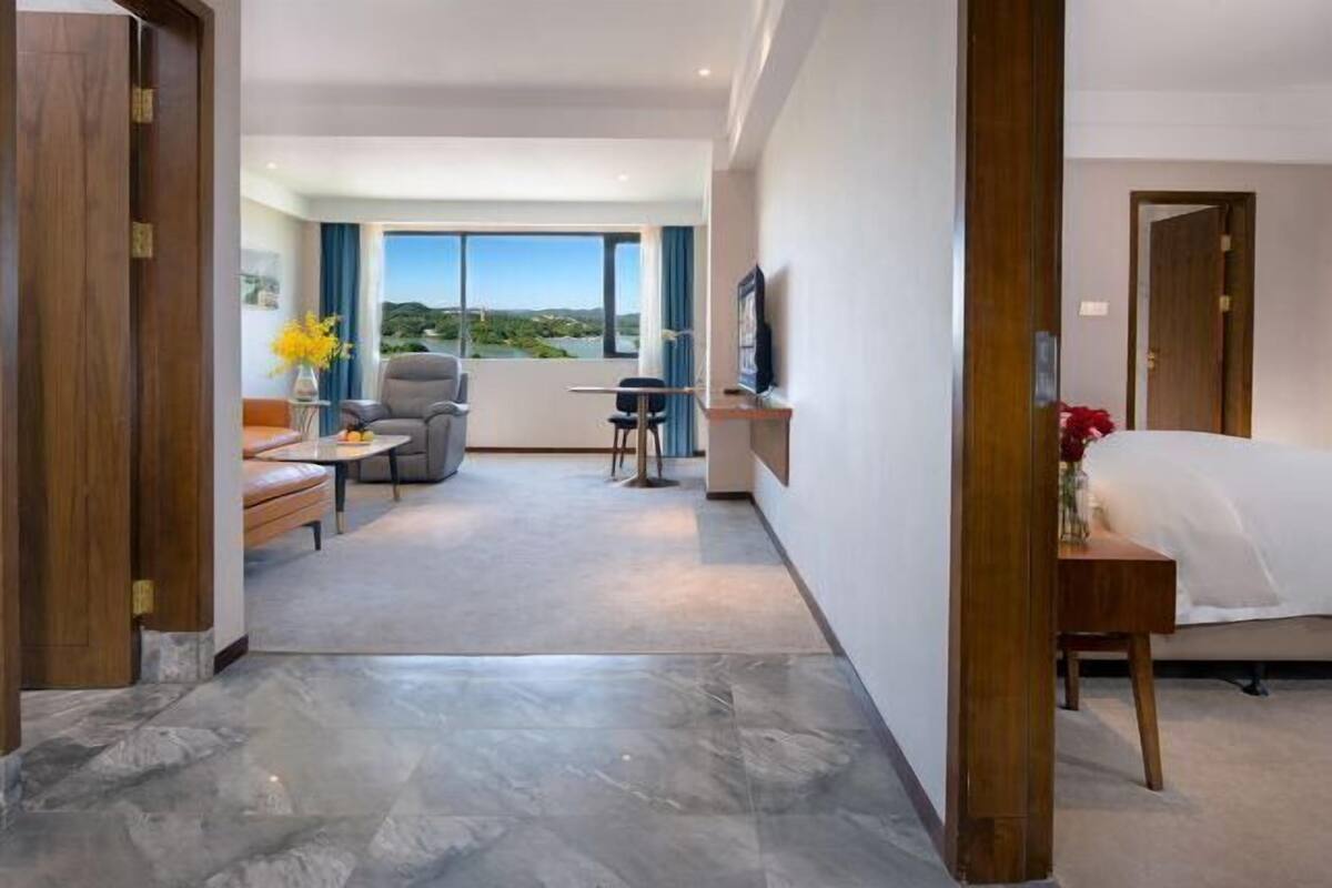 Habitación de hotel con cama, escritorio, silla, televisor y vistas al exterior.