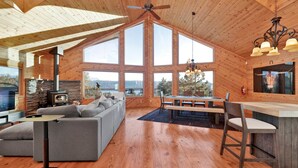 A spacious living area with a fireplace, large windows, and a high ceiling.