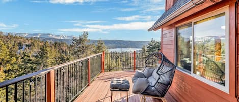 A wooden deck with a black chair and ottoman, a glass door, and a view of a forest and mountains.