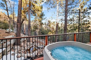 Un jacuzzi rodeado por una terraza de madera con barandillas metálicas, con vista a una zona rocosa con pinos.