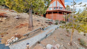 A wooden cabin with a steep driveway and a stone pathway leading to the entrance.