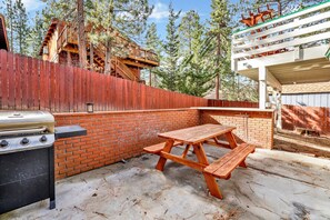 A backyard with a barbecue grill, a picnic table, and a wooden fence.