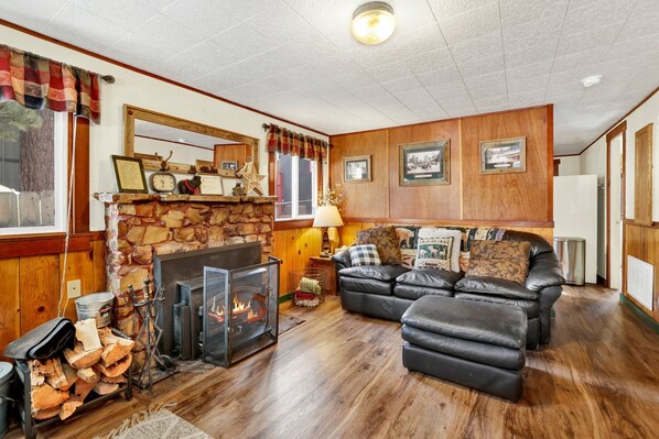 A cozy living room with a stone fireplace, a black leather sofa, and a wooden floor.