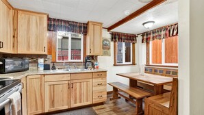 A kitchen with wooden cabinets, a microwave, a sink, and a window with a view of a red fence. - Green Squirrel Chateau #2484 (Big Bear Lake)