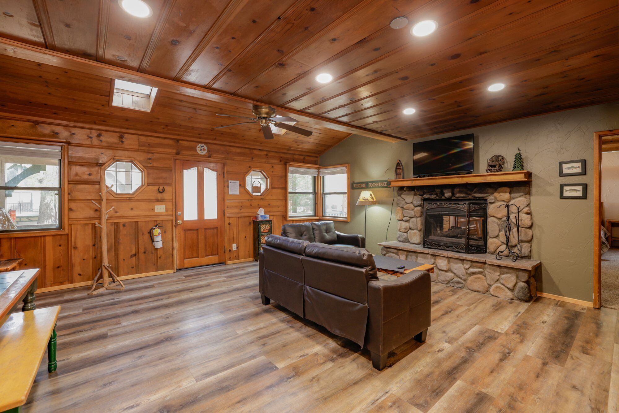 A cozy cabin interior with a stone fireplace, wooden walls, and a leather sofa.