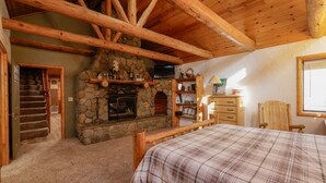 Una habitación acogedora con chimenea de piedra, vigas de madera, una cama, un aparador y un televisor.