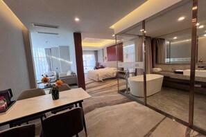 A modern hotel room with a dining area, a large bed, a glass-enclosed bathroom, and a view of the city. - Rishengchang Hotel (Beijing South Railway Station) (Beijing)