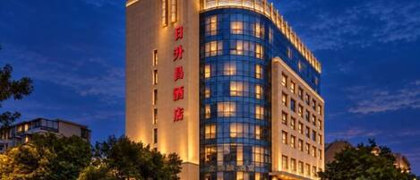 A multi-story hotel with a prominent vertical sign on the left and a curved facade on the right.