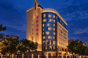 Un hotel de varios pisos con un letrero vertical llamativo a la izquierda y una fachada curva a la derecha.