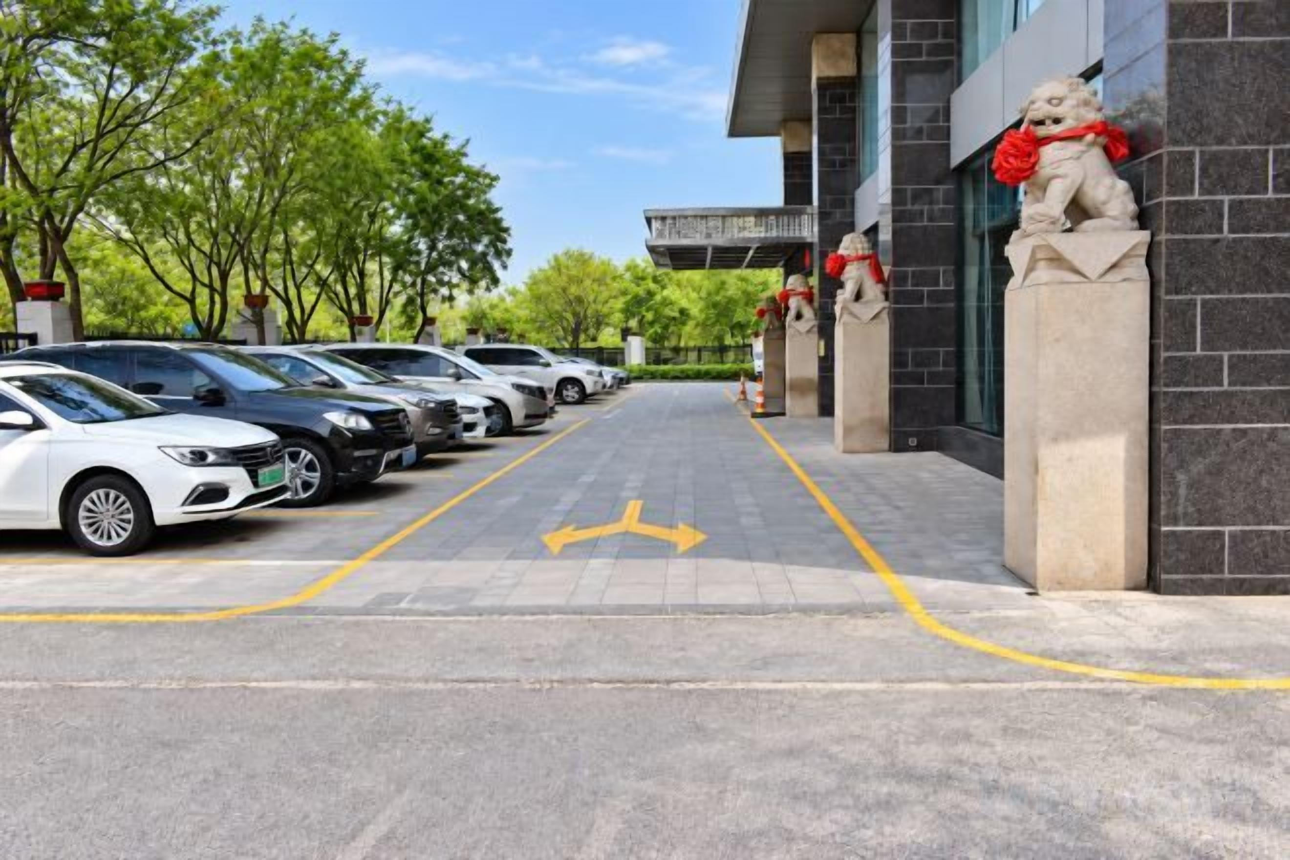A parking lot with cars parked in rows, a building entrance with a lion statue, and a clear sky.