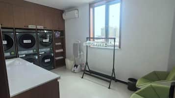 A laundry area with multiple washing machines, a drying rack, and a window with a view.