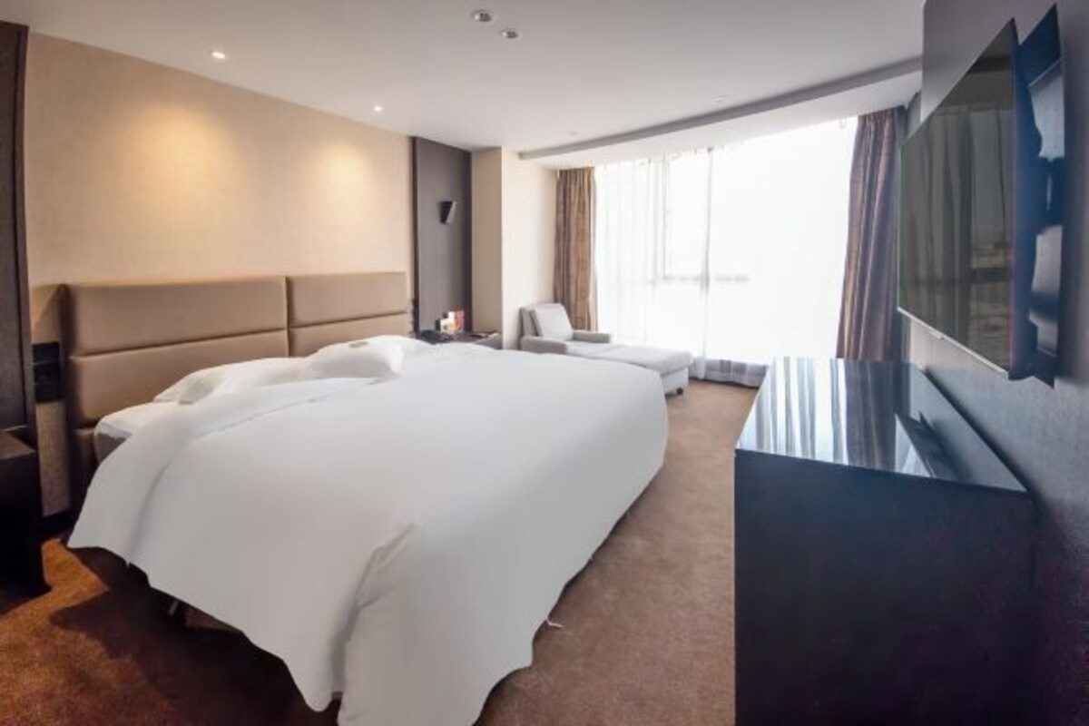 A hotel room with a large bed, a TV, a desk, and a window with curtains.