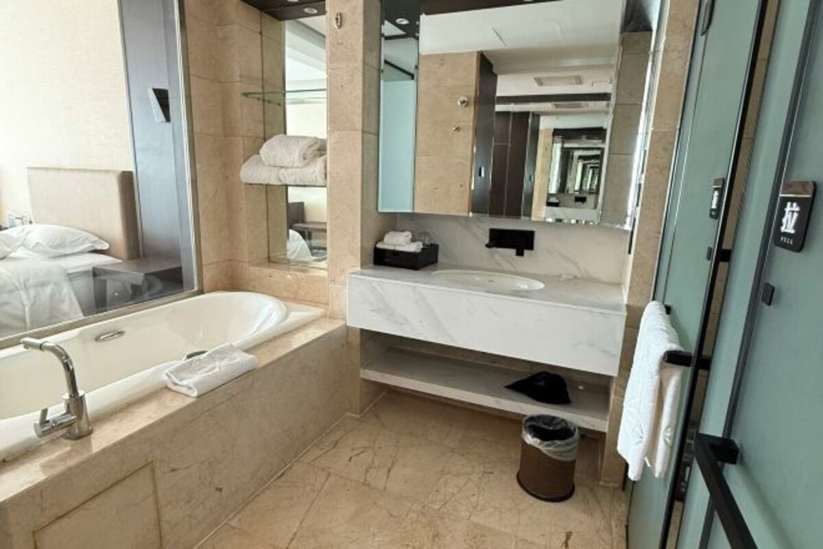 A modern bathroom with a large bathtub, a vanity with a mirror, and a trash bin.