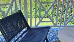 A balcony with a wicker chair and a small table, overlooking a lush landscape and the ocean. - ✨ Suite de Charme avec Vue Mer - Havre de Paix en Martinique 🌴🌊 (Trois-Ilets)