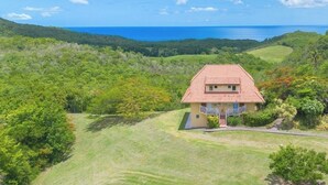 A single-story house with a red-tiled roof, surrounded by lush greenery and a clear view of the ocean. - ✨ Suite de Charme avec Vue Mer - Havre de Paix en Martinique 🌴🌊 (Trois-Ilets)