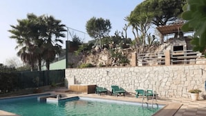 A swimming pool with a stone wall and green chairs. - Villas Coliving Casa Rural (Sant Fost de Campsentelles)