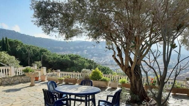 A patio with a stone table and chairs, surrounded by potted plants and a view of a mountainous landscape. - Villas Coliving Casa Rural (Sant Fost de Campsentelles)