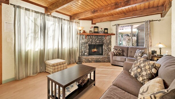 A cozy living room with a stone fireplace, wooden ceiling beams, a sofa, and a coffee table.