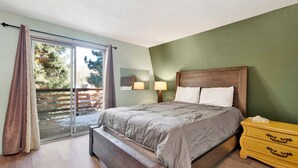 A bedroom with a bed, a nightstand, a lamp, and a sliding glass door leading to a balcony.