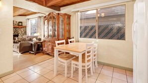 A cozy dining area with a wooden table and chairs, a cabinet with glass doors, and a large window with a view of a roof.