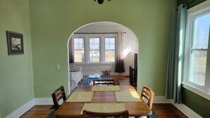 Un coin repas avec une table en bois, des chaises et une vue, par une porte en arc de cercle, sur un salon comprenant un canapé et une fenêtre.