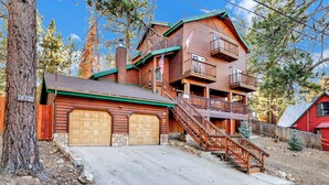 Une cabane en rondins à deux étages, avec un garage à l’avant, un balcon au deuxième étage et un escalier menant à l’entrée principale.