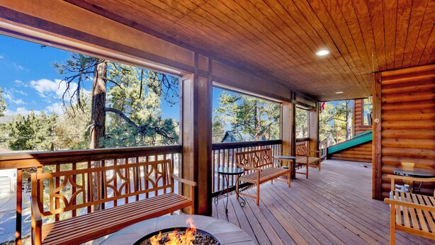 Une terrasse en bois avec un foyer, des bancs et une vue sur les arbres.