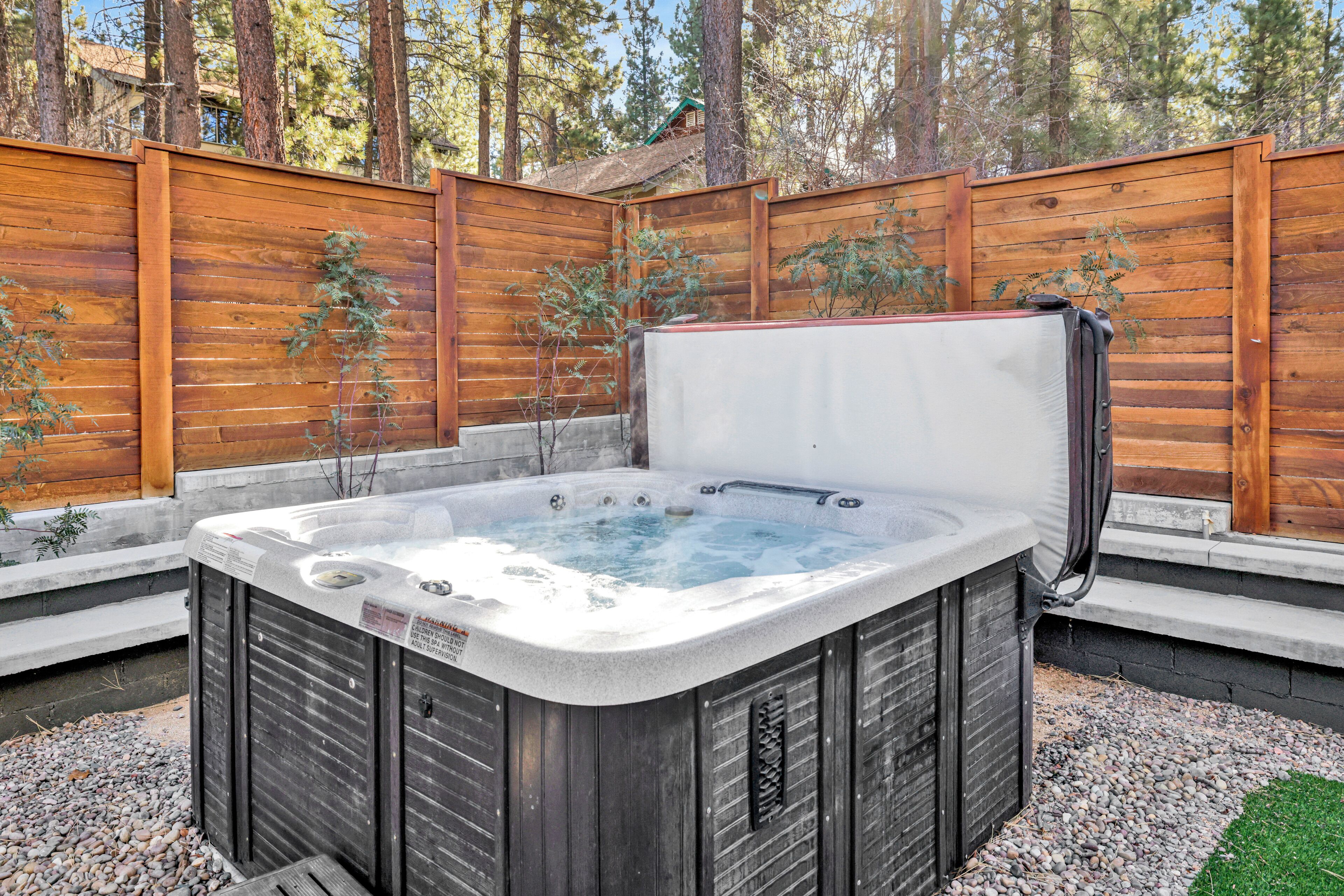 A hot tub in a backyard with a wooden fence and trees in the background.