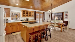 Une cuisine spacieuse avec des meubles en bois, un grand îlot central doté de tabourets, et un coin repas avec des chaises et une table.