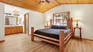 Une chambre à coucher avec un lit en bois, deux tables de chevet avec des lampes, un ventilateur de plafond et une grande fenêtre avec des rideaux.
