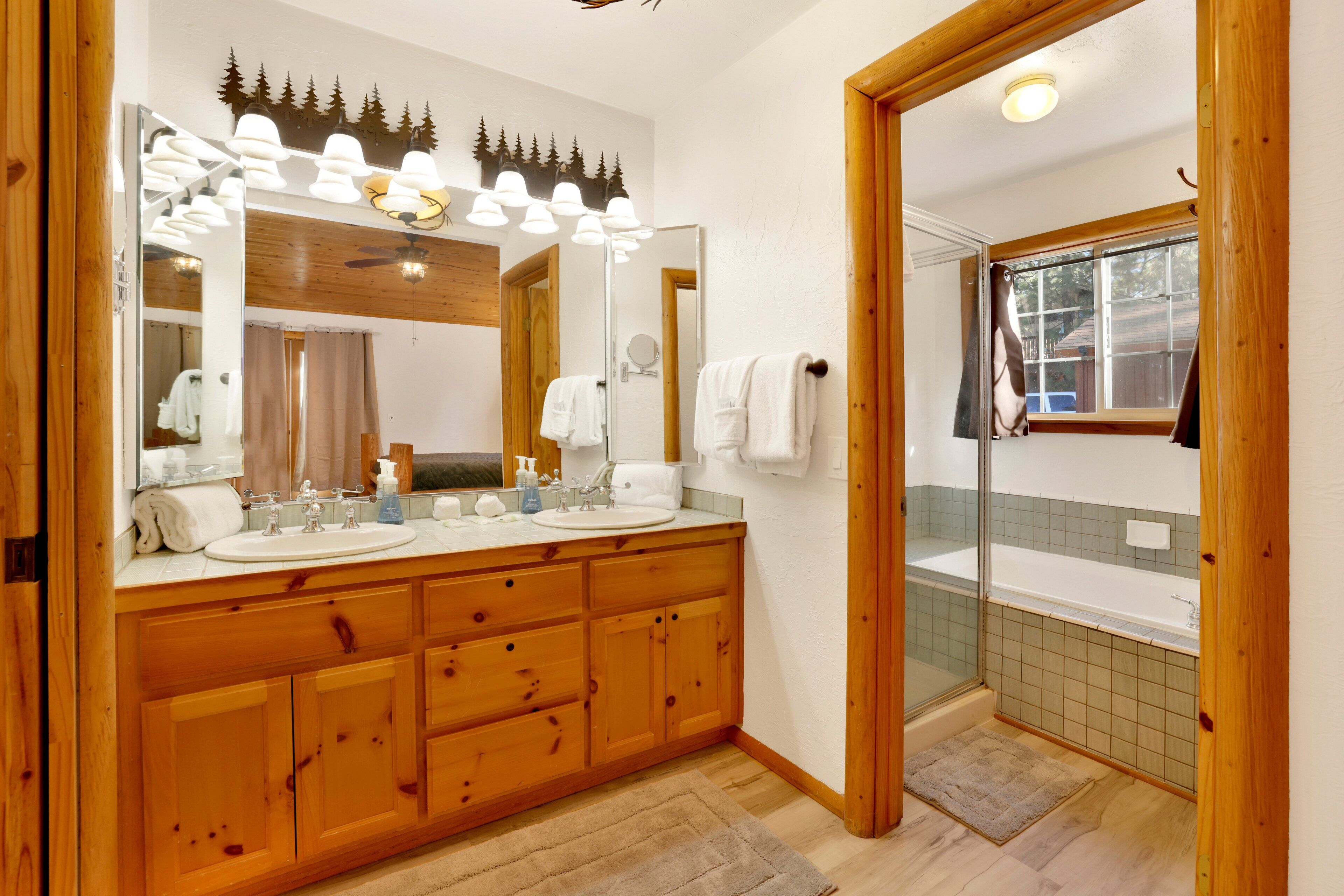 Un baño de madera con dos lavamanos, un espejo grande y una ducha con mampara de vidrio.