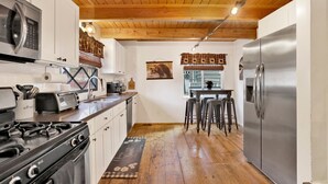 A kitchen with white cabinets, a stainless steel refrigerator, a stove, and a wooden ceiling. - Camp Conklin #2337 (Big Bear Lake)