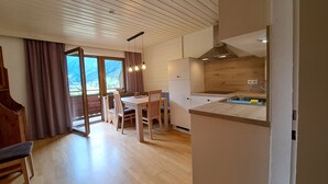 A modern kitchen with wooden cabinets, a dining area with a table and chairs, and a view of mountains through the window. - Haus Kaunergrat (Kaunertal)