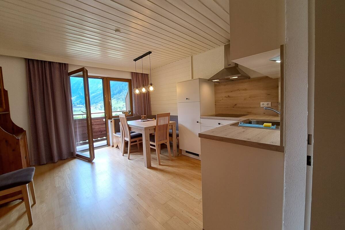 A modern kitchen with wooden cabinets, a dining area with a table and chairs, and a view of mountains through the window.