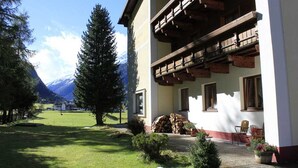 A traditional chalet with a wooden balcony, a stone fireplace, and a view of a mountain range. - Haus Kaunergrat (Kaunertal)