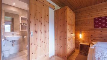A wooden interior with a bathroom on the left, a bed on the right, and a wooden door in the center.