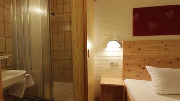 A bathroom with a shower, sink, and a wooden bedside table with a bed.