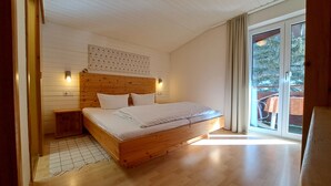 A bedroom with a wooden bed, a nightstand, a wall-mounted light, and a large window with curtains. - Haus Kaunergrat (Kaunertal)