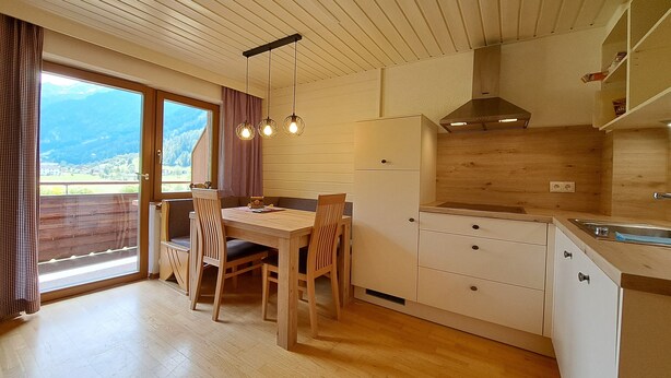 A modern kitchen with wooden cabinets, a dining area with a table and chairs, and a view of the mountains through the window. - Haus Kaunergrat (Kaunertal)