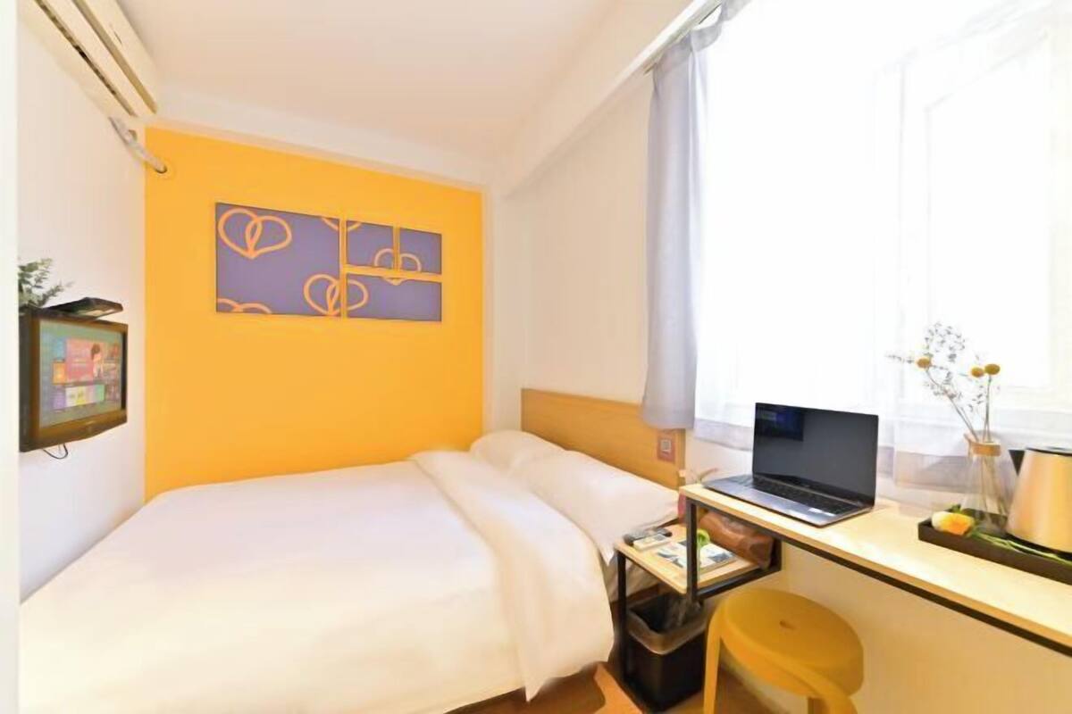 A hotel room with a bed, a desk with a laptop, a chair, and a window with curtains.