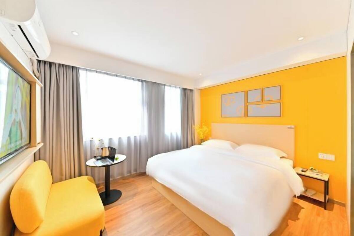 A hotel room with a bed, a small table, a chair, and a window with curtains.