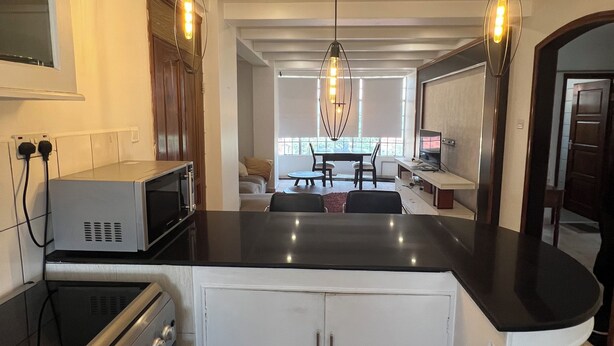 A modern kitchen with a central island, stainless steel appliances, pendant lighting, and a view into the living area.