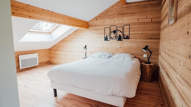 A bedroom with a sloped ceiling, wooden walls, a skylight, a bed, bedside lamps, and a framed picture on the wall. - L'Ecureuil apartment, Finnish bath on the edge of the forest. Pets allowed (Gérardmer)