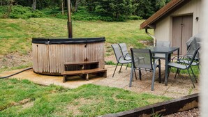 A hot tub with a wooden exterior, surrounded by a patio area with a table and chairs. - L'Ecureuil apartment, Finnish bath on the edge of the forest. Pets allowed (Gérardmer)